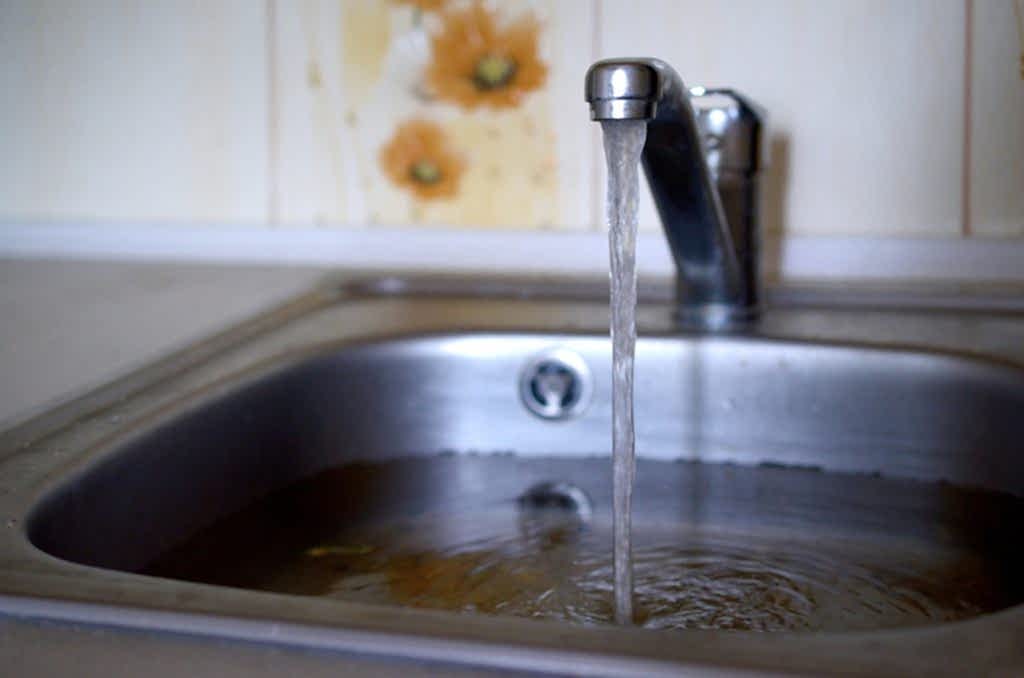 Stainless steel sink plug hole close up full of water and particles of food